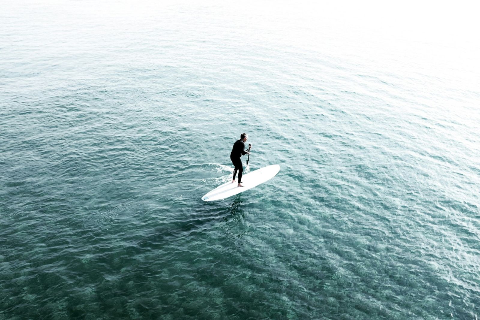 A man in a wetsuit stand-up paddleboarding on calm, clear water